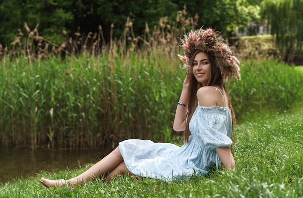 Mujer morena con vestido azul y corona de flores sentada al lado del lago