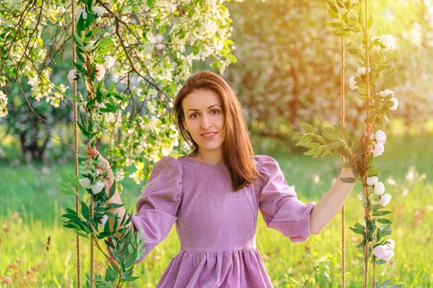 Una mujer morena con un vestido morado posa en un columpio de cuerda en un parque en primavera