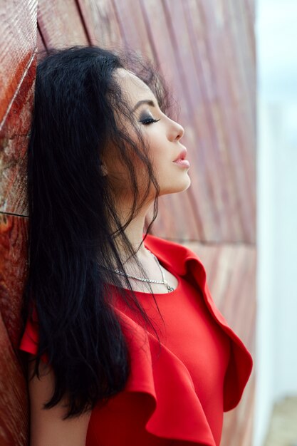 mujer morena con un vestido rojo está de pie cerca de la puerta roja.