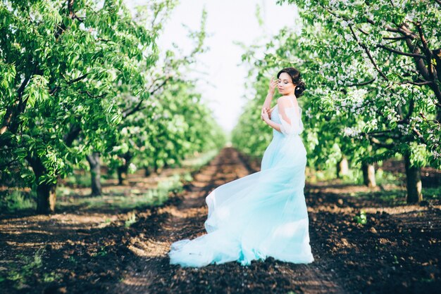 Mujer morena con un vestido turquesa caminando en el jardín de primavera