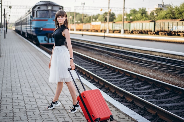 Mujer morena viajero con maleta roja caminando en la estación de ferrocarril