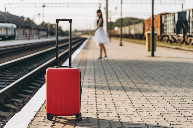 Mujer morena viajero con maleta roja caminando en la estación de ferrocarril