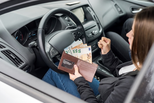 Mujer mostrando los billetes en euros en la billetera sentado en el coche