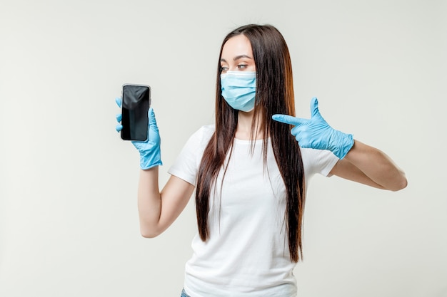 Mujer mostrando copia vacía pantalla del teléfono con máscara y guantes