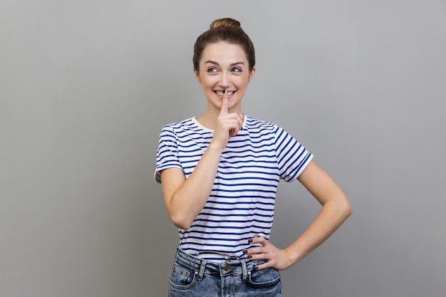 Mujer mostrando gesto shh sosteniendo el dedo cerca de los labios con una sonrisa traviesa en la cara haciendo sorpresa en secreto