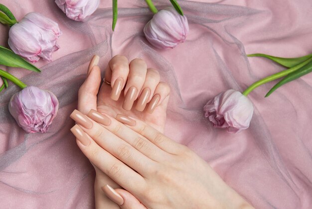 Mujer mostrando una manicura desnuda en un fondo rosa con tulipanes