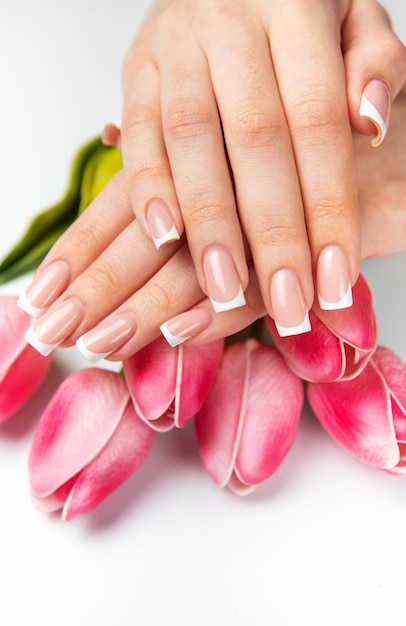 Mujer mostrando manicura francesa y tulipanes rosados sobre un fondo blanco