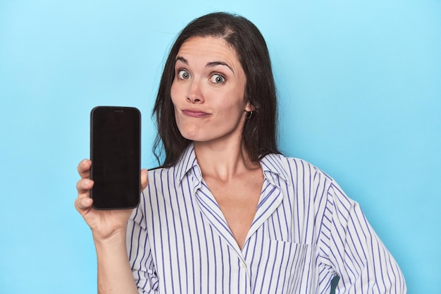 Mujer mostrando la pantalla del teléfono sobre fondo azul