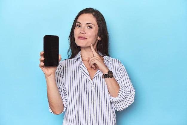 Foto mujer mostrando la pantalla del teléfono sobre fondo azul