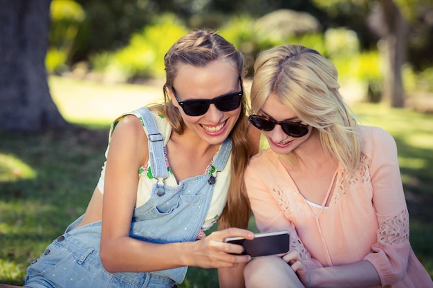 Mujer mostrando teléfono móvil a su amiga