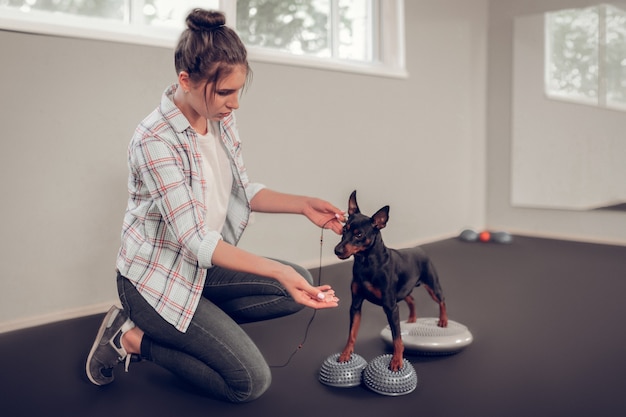 Mujer mostrando tocino. Mujer morena entrenando a su perro negro mostrándole un trozo de tocino