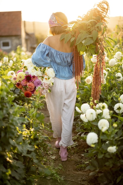 Mujer con muchas flores en la granja de dahlia al aire libre