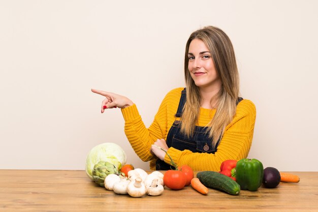 Mujer con muchas verduras apuntando con el dedo hacia un lado.