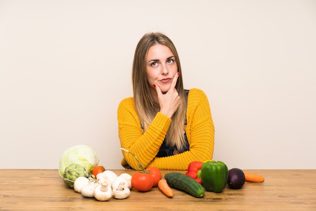 Mujer con muchas verduras de pie y pensando en una idea