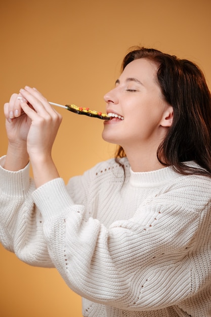 Mujer muerde piruleta dulce con dientes blancos sobre fondo amarillo concepto de comida dulce para el nuevo año