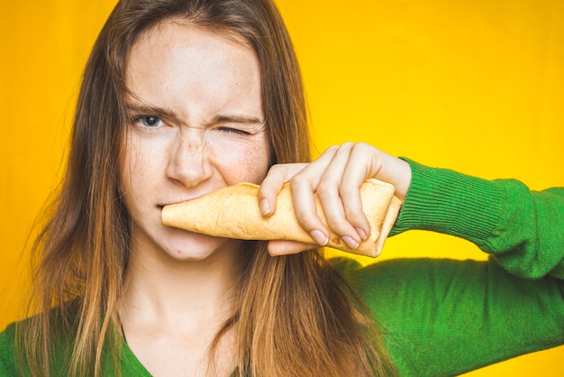 La mujer muerde el sándwich. Come alimentos poco saludables.