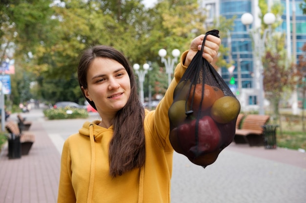 La mujer muestra una bolsa de tela transparente negra con fruta.