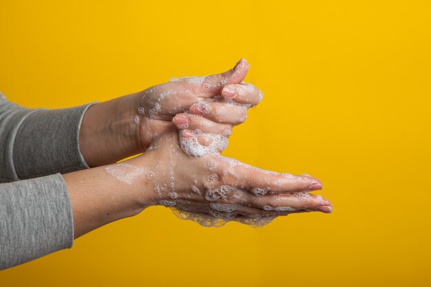 La mujer muestra cómo lavarse las manos con jabón. pared amarilla brillante, aislada. desinfección de manos para prevenir la enfermedad por coronavirus.