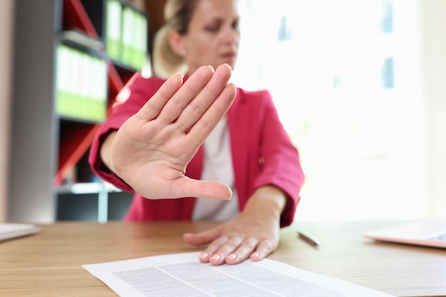 La mujer muestra un gesto de rechazo con la palma sentada en una mesa de madera en la oficina mujer irritada