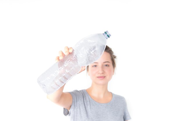 La mujer muestra y que sostiene la botella plástica reciclable aislada en el fondo blanco.