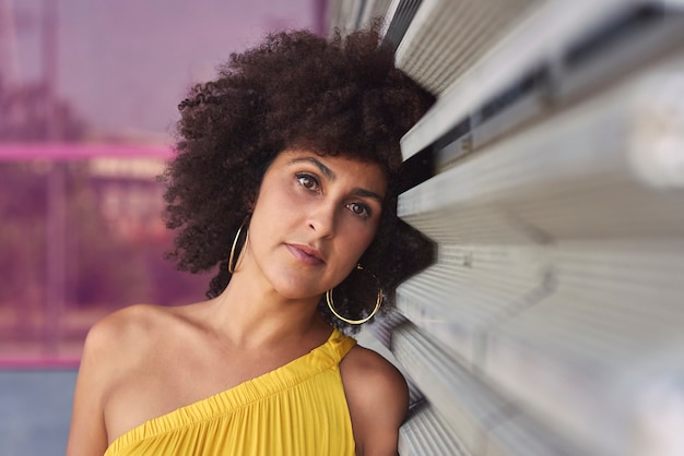 Mujer mulata de pelo afro con un vestido amarillo y fondo morado.