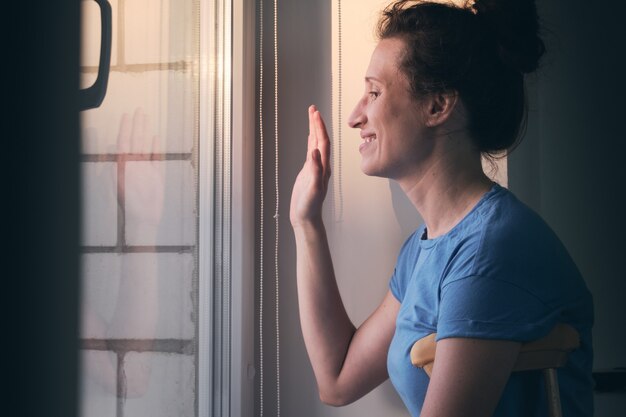 Mujer con muletas se encuentra en la ventana y agita su mano