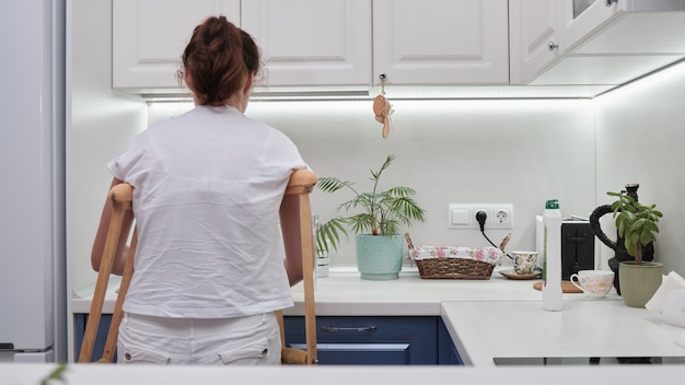 Mujer con muletas lava los platos en la cocina