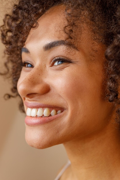 Mujer multiétnica con dientes sonriendo sobre fondo beige de estudio