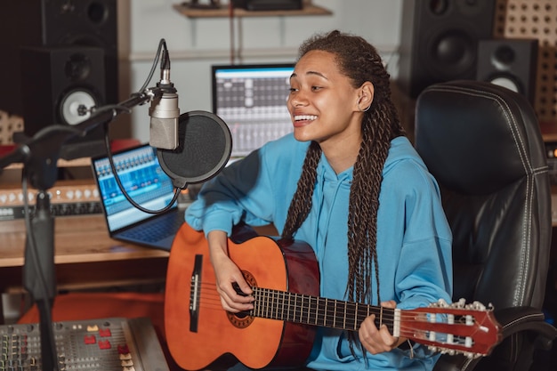 Foto mujer multirracial músico cantante compositora guitarrista y compositora ensayando una nueva pista genial en el estudio de grabación de sonido