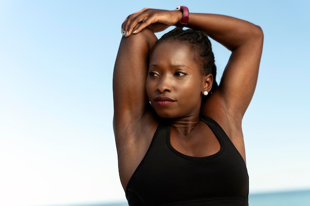 Mujer multirracial en ropa deportiva haciendo ejercicio al aire libre y calentándose en la playa