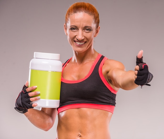 Mujer muscular sonriente con el tarro de proteína.