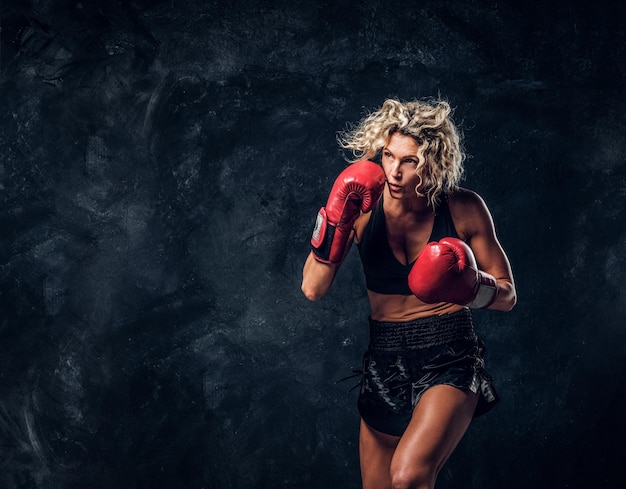 Foto mujer musculosa deportiva está demostrando sus ejercicios de boxeo, usando guantes.