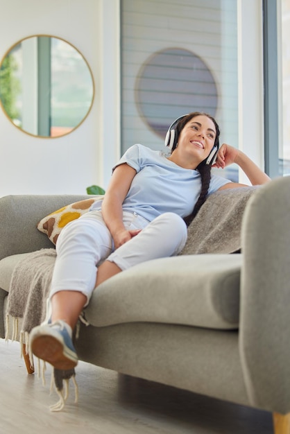 Mujer música y relajación con auriculares en el sofá en la sala de estar para la felicidad escuchando podcast y paz en casa Sonrisa feliz y transmisión de radio en el sofá para aliviar el estrés o calmar el bienestar