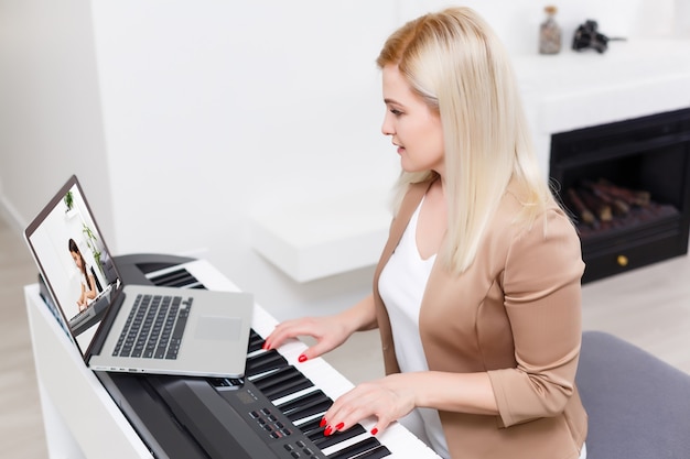 Mujer músico tocando el piano digital clásico en casa durante la clase en línea en casa, distancia social durante la cuarentena, autoaislamiento, concepto de educación en línea