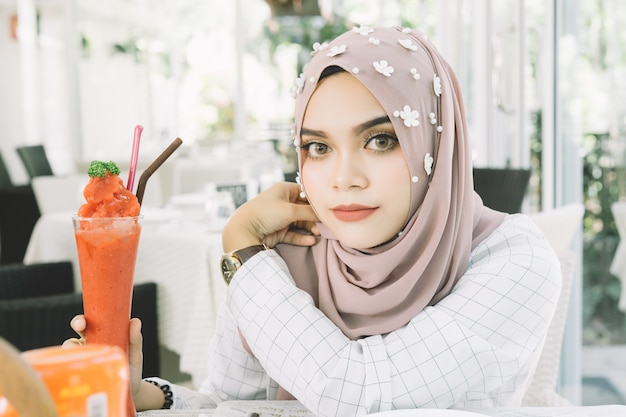 Mujer musulmán hermosa joven con el smoothie de la fresa en restaurante.