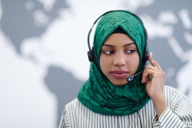 Mujer musulmana africana con bufanda hijab verde representante del cliente mujer de negocios con auriculares de teléfono ayudando y apoyando en línea con el cliente en un centro de llamadas moderno