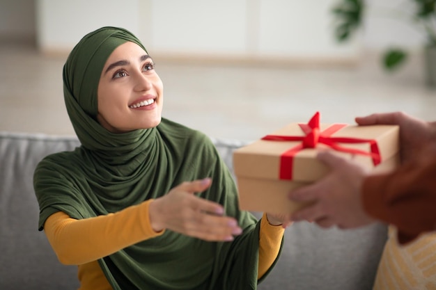 Mujer musulmana alegre con hiyab recibiendo caja de regalo en casa