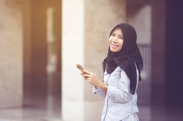 Mujer musulmana alegre sonriendo a la cámara con teléfono