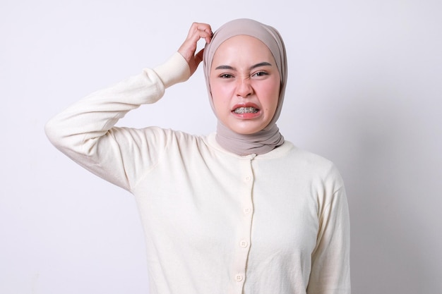 Foto mujer musulmana con aparatos ortopédicos rascándose la cabeza y mostrando una expresión confusa