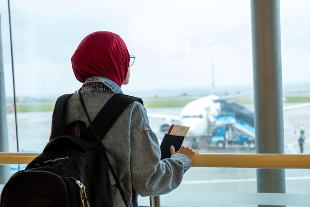 Mujer musulmana árabe en el aeropuerto sosteniendo su pasaporte y mirando el avión