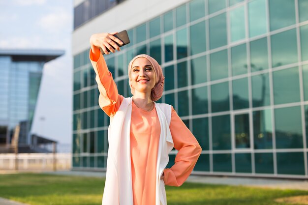 Mujer musulmana árabe tomando selfie en smartphone al aire libre