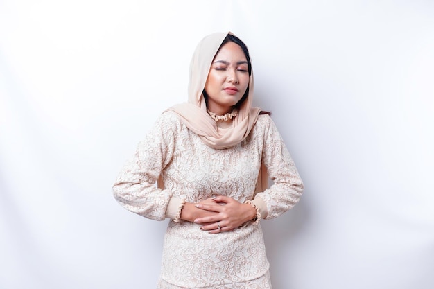 Una mujer musulmana asiática ayuna y tiene hambre y se toca el vientre mientras mira a un lado pensando en qué comer