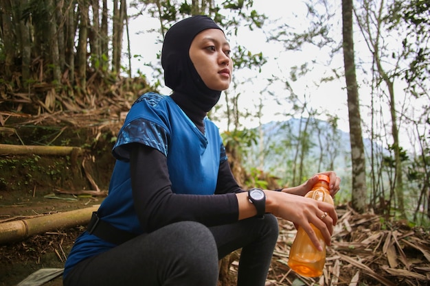 Mujer musulmana asiática bebiendo agua después de correr, salud y concepto de deporte.