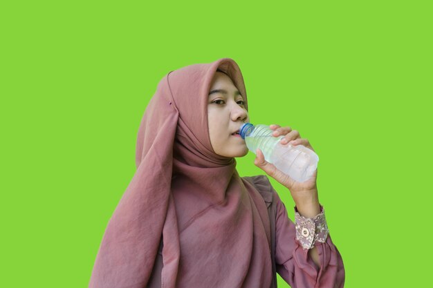 Mujer musulmana asiática bebiendo agua embotellada con fondo verde