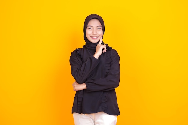 Mujer musulmana asiática con el dedo índice en la mejilla sonriendo muy lindamente
