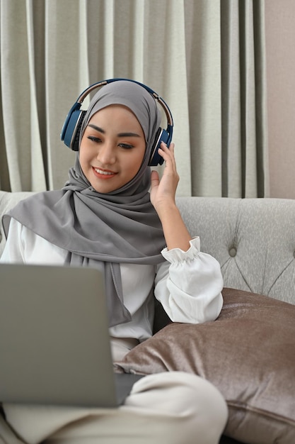 Mujer musulmana asiática con hiyab y auriculares viendo una película en una laptop