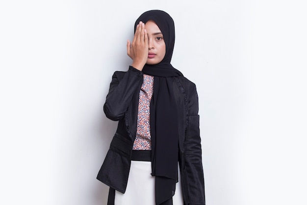 Mujer musulmana asiática joven que cubre un ojo con la mano aislada en el fondo blanco