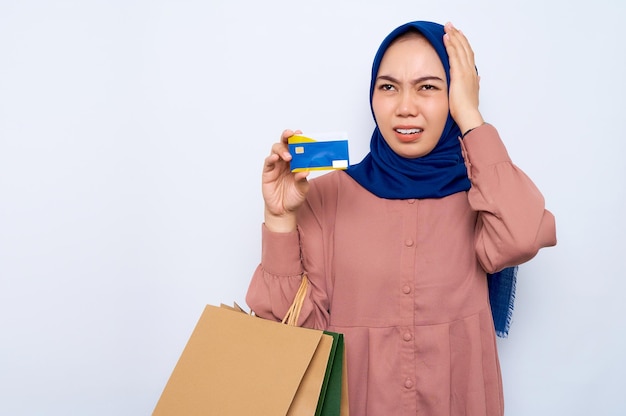 Mujer musulmana asiática joven sorprendida en camisa rosa sosteniendo bolsas de paquetes con compras después de compras y tarjeta de crédito bancaria aislada sobre fondo blanco Concepto de estilo de vida de la gente