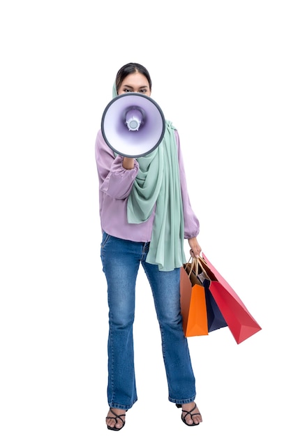 Mujer musulmana asiática con un pañuelo en la cabeza sosteniendo un megáfono y bolsas de compras