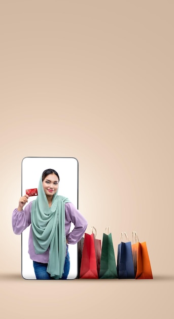 Mujer musulmana asiática con un pañuelo en la cabeza sosteniendo una tarjeta de crédito en la pantalla de un teléfono móvil